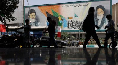 Pessoas caminham ao lado de um mural com uma foto do líder supremo do Irã, aiatolá Ali Khamene...